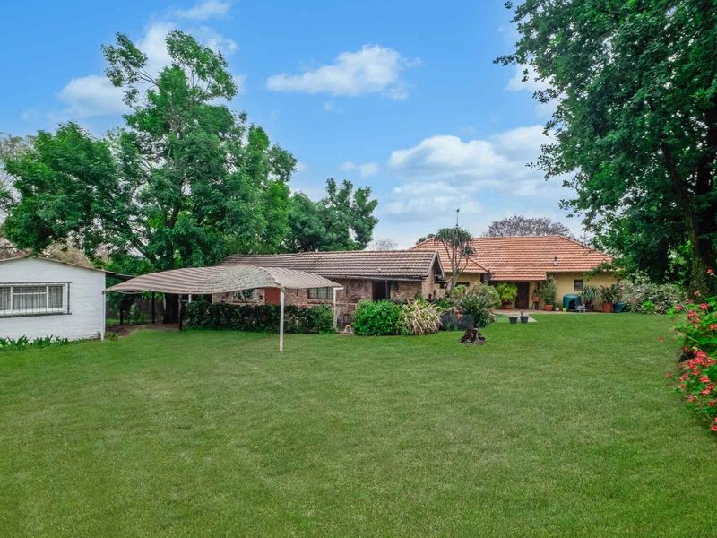 A view of the rear exterior of the farm property, featuring a spacious lawn, mature trees, and a covered patio area.