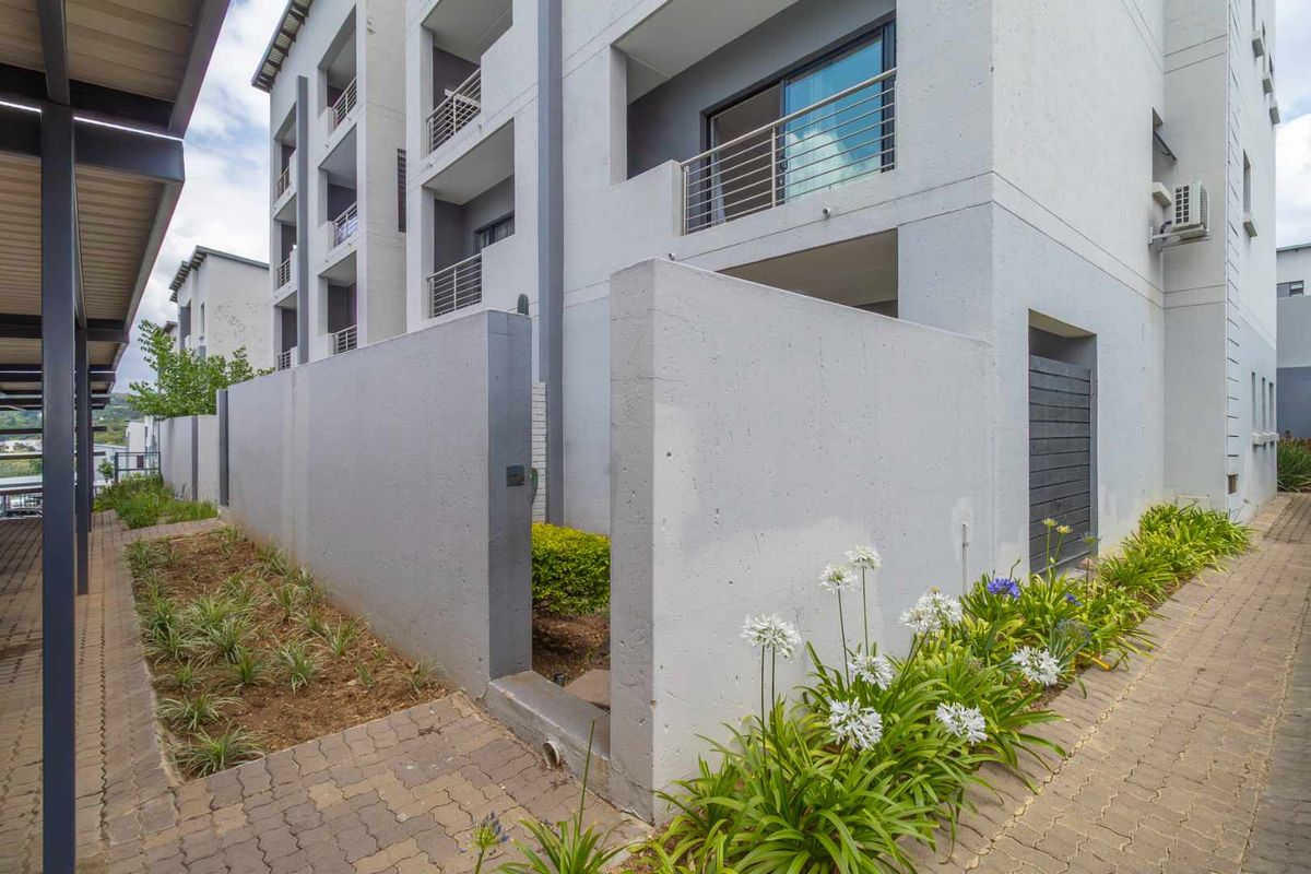 Exterior view of a modern apartment building featuring concrete boundary walls, paved walkways, and private balcony access.