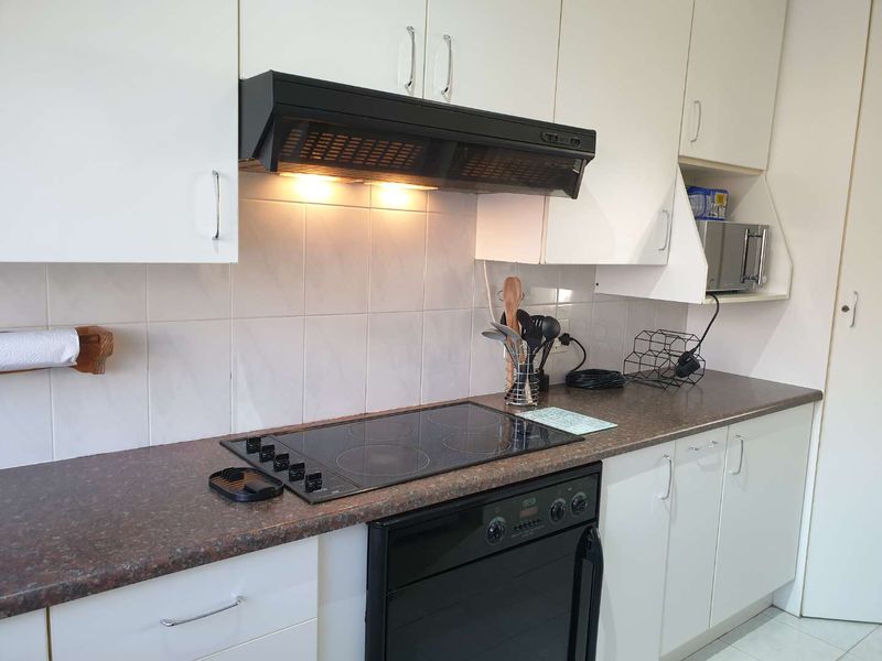 A functional kitchen featuring white cabinetry, a dark laminate countertop, tiled backsplash, and integrated electric cooking appliances.