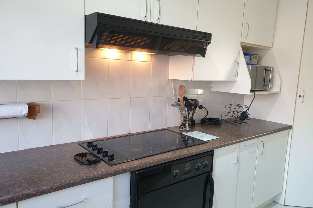 A functional kitchen featuring white cabinetry, a dark laminate countertop, tiled backsplash, and integrated electric cooking appliances.