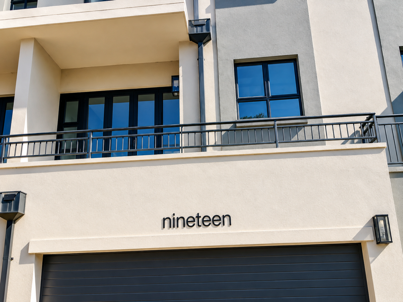 Modern residential facade featuring a sectional garage door, metal balcony railing, and contemporary exterior lighting.