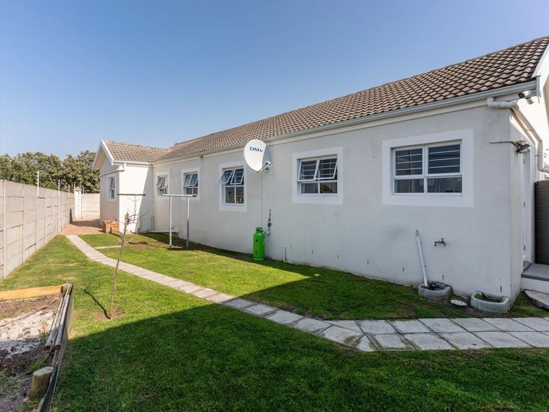 Rear exterior view of the property featuring a paved walkway, lawn, concrete boundary wall, and water tank.