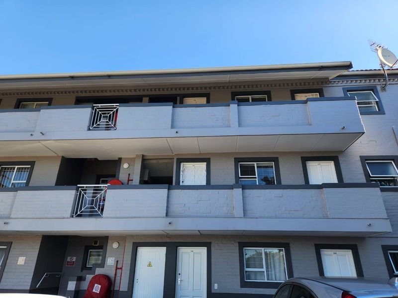 Exterior view of a multi-story apartment building featuring grey painted brick facade, private balconies with metal railings, and multiple entry points.