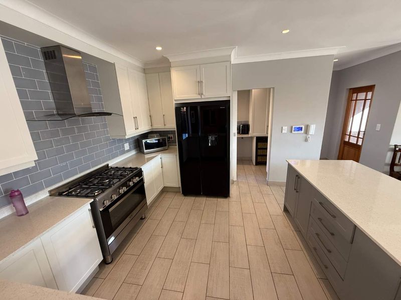 Modern kitchen featuring white cabinetry, stone countertops, a central island, subway tile backsplash, and a gas stove with stainless steel extractor fan.