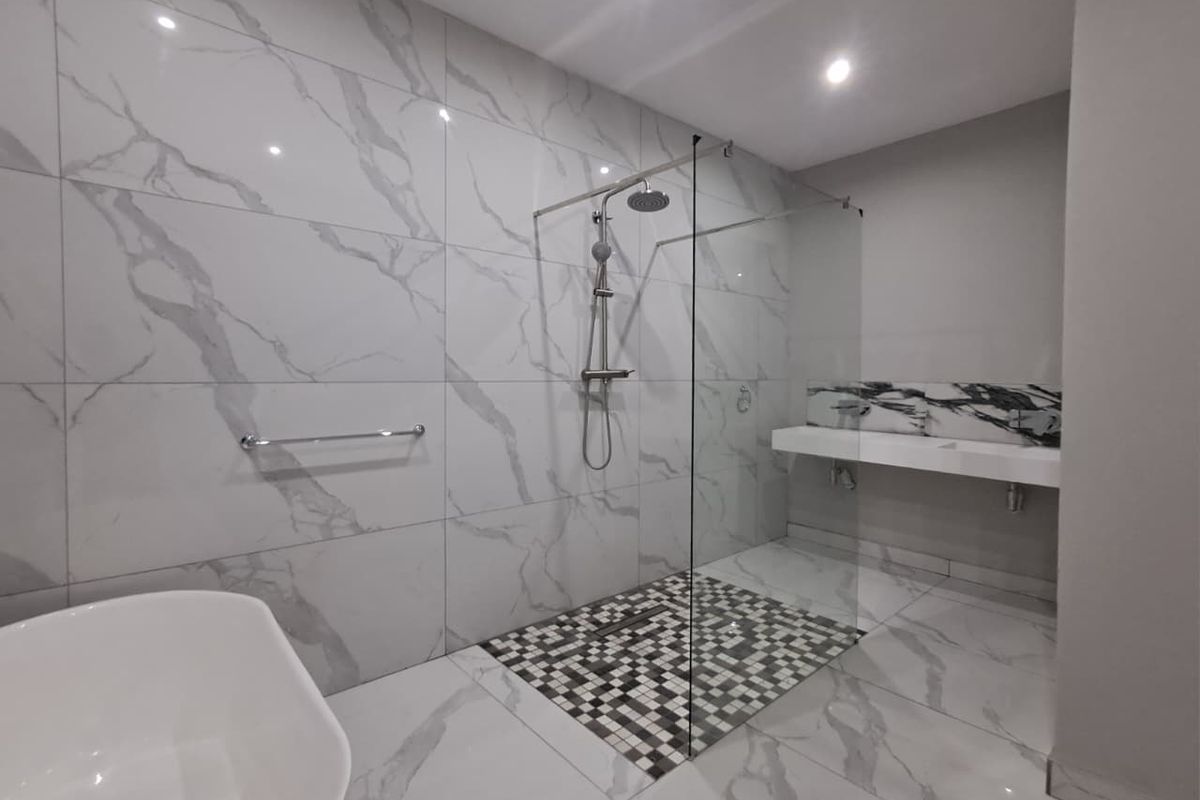Modern bathroom featuring a large walk-in shower with glass screen, marble-look wall tiles, a freestanding bathtub, and a sleek wall-mounted double vanity.