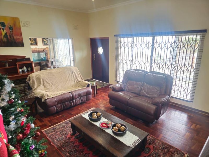 A living room featuring classic parquet flooring, a fireplace, and large sliding glass doors with security gates providing natural light.