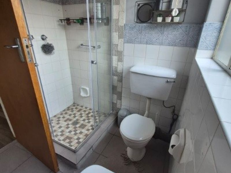 A functional bathroom featuring a glass-enclosed shower, standard toilet, and washbasin with tiled walls and flooring.