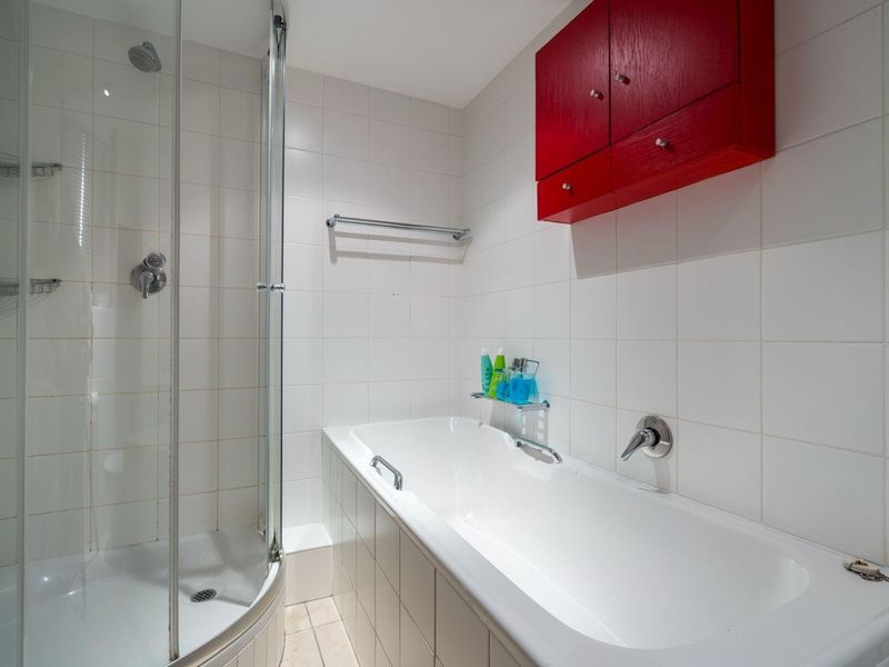 A functional bathroom featuring a separate shower enclosure, a built-in bathtub, and white wall tiling with a contrasting red wall-mounted cabinet.