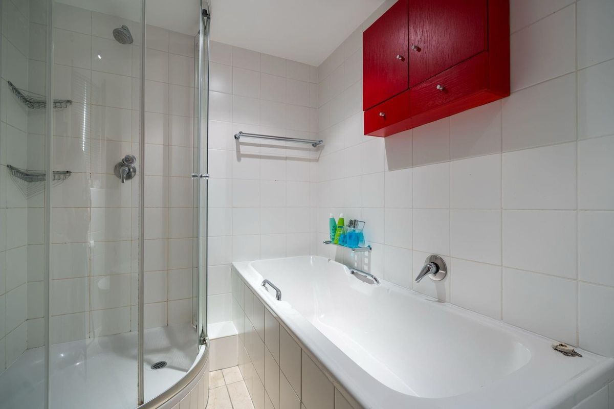 A functional bathroom featuring a separate shower enclosure, a built-in bathtub, and white wall tiling with a contrasting red wall-mounted cabinet.