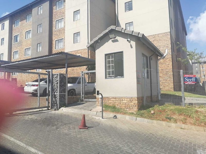 Entrance view of the townhouse complex featuring a security guard house, gated access control, and covered parking area.