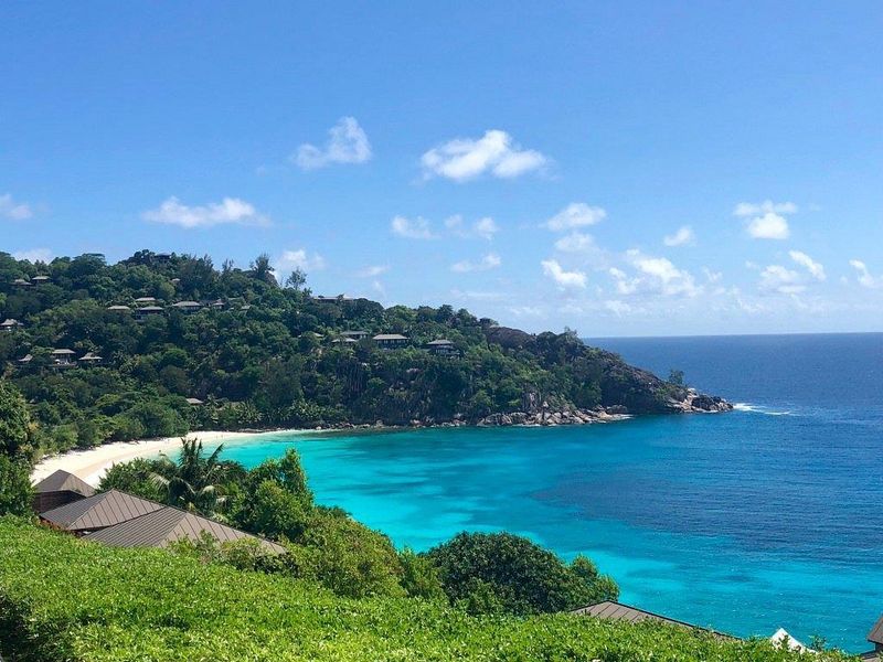 A stunning elevated view overlooking a pristine tropical coastline with turquoise waters, white sandy beach, and lush hillside vegetation.