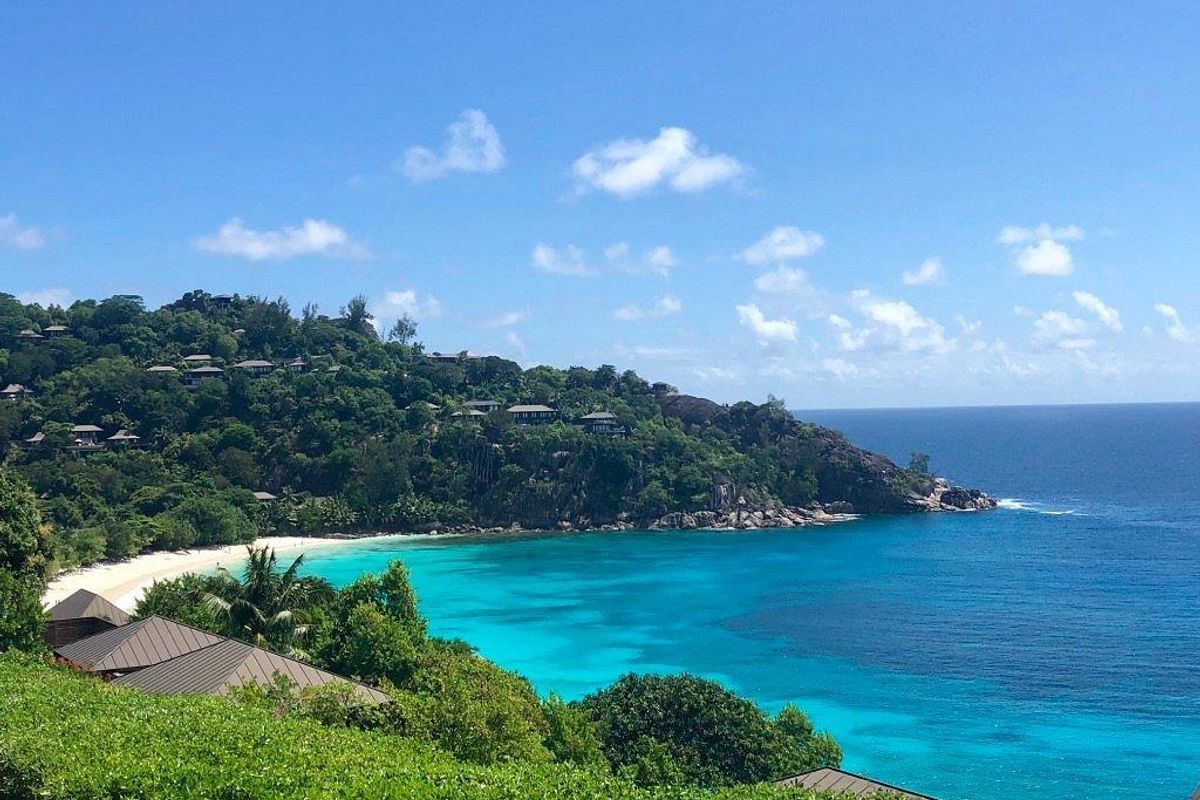 A stunning elevated view overlooking a pristine tropical coastline with turquoise waters, white sandy beach, and lush hillside vegetation.