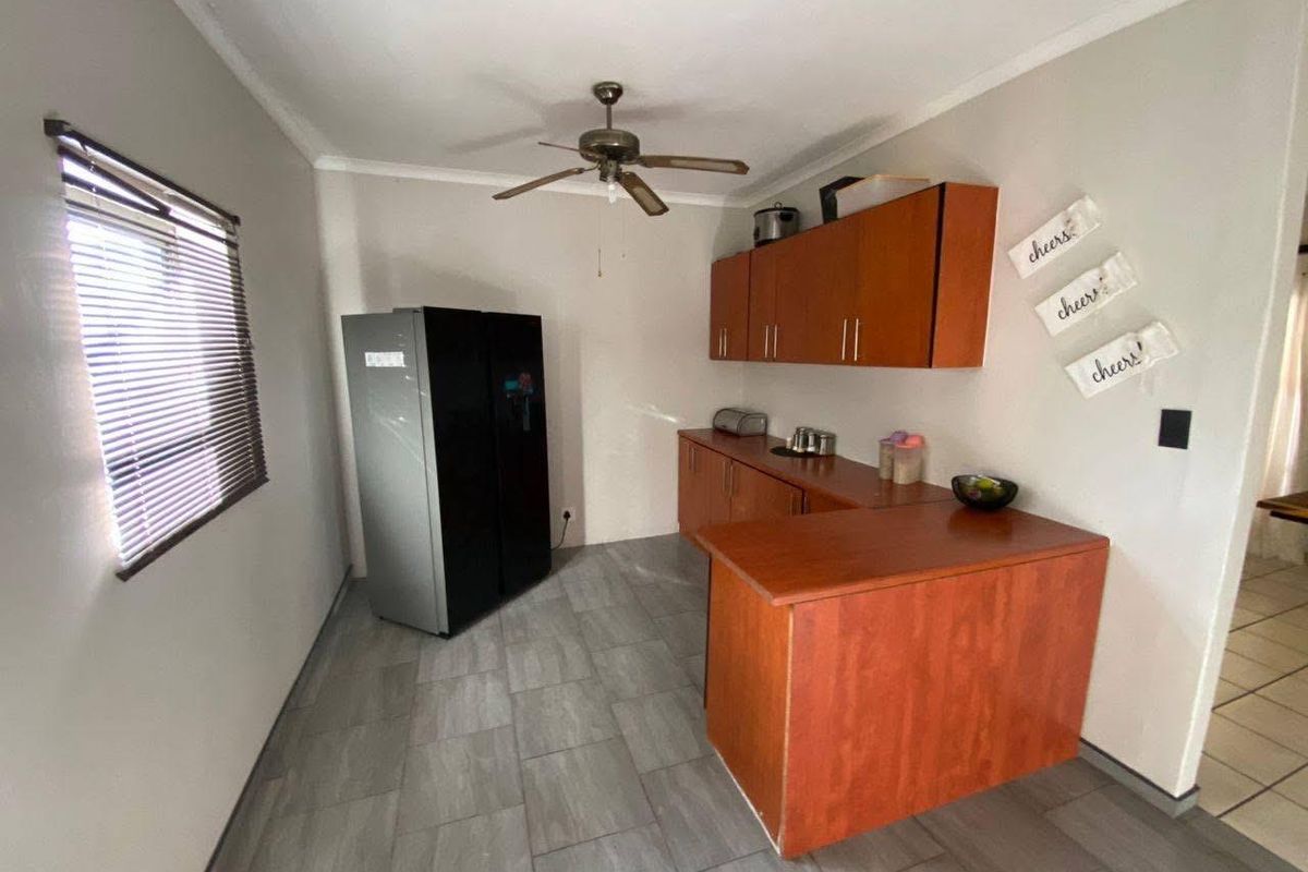 A functional kitchen area featuring wood-finish cabinetry, a breakfast counter, tiled flooring, and a ceiling fan.