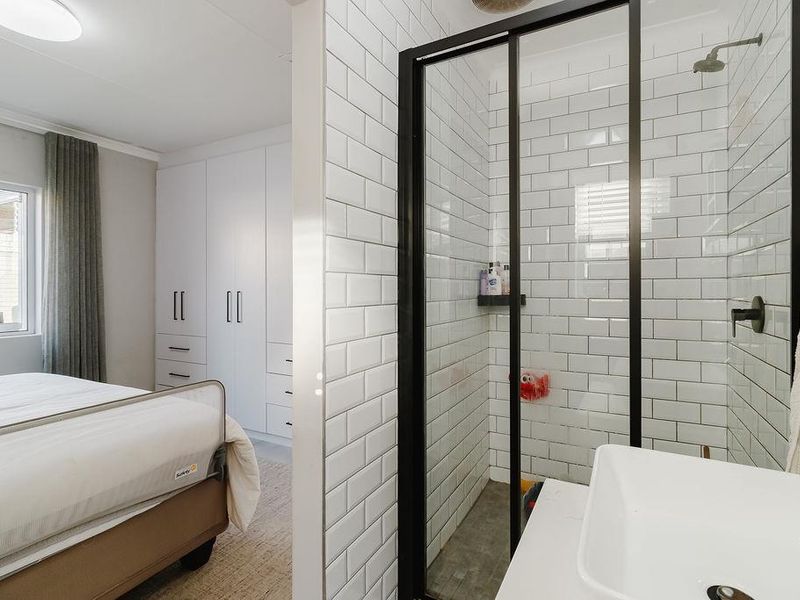 A modern bedroom featuring built-in cupboards and an en-suite bathroom with a contemporary subway-tiled shower and vessel sink.