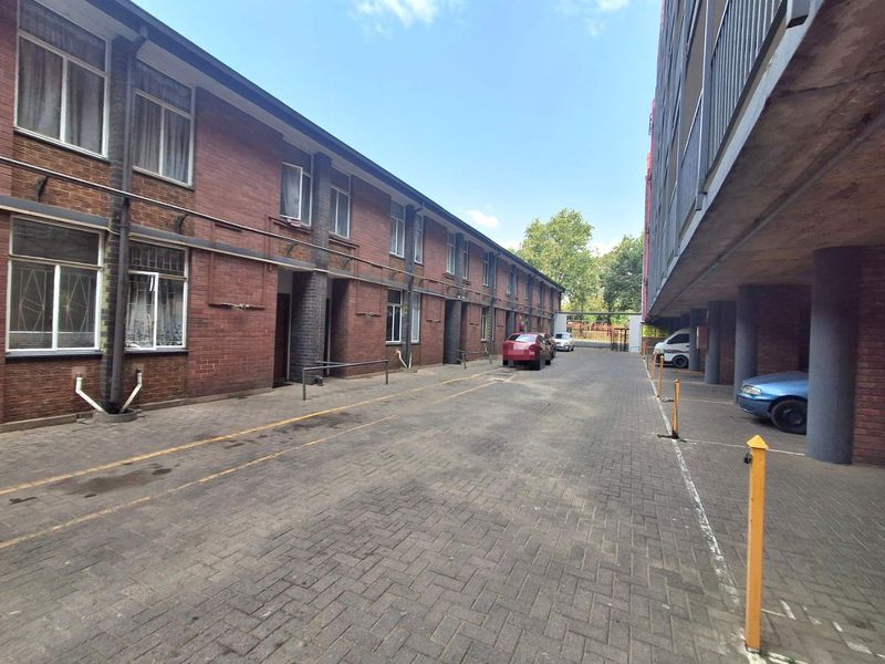 Exterior view of an apartment complex featuring a brick facade, paved driveway, and covered parking area.