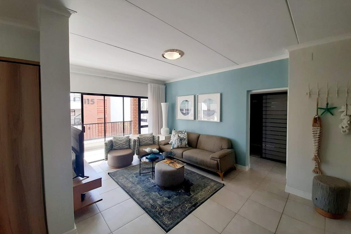 A bright living room featuring tiled flooring, a feature wall, and large sliding glass doors that open onto a private balcony.