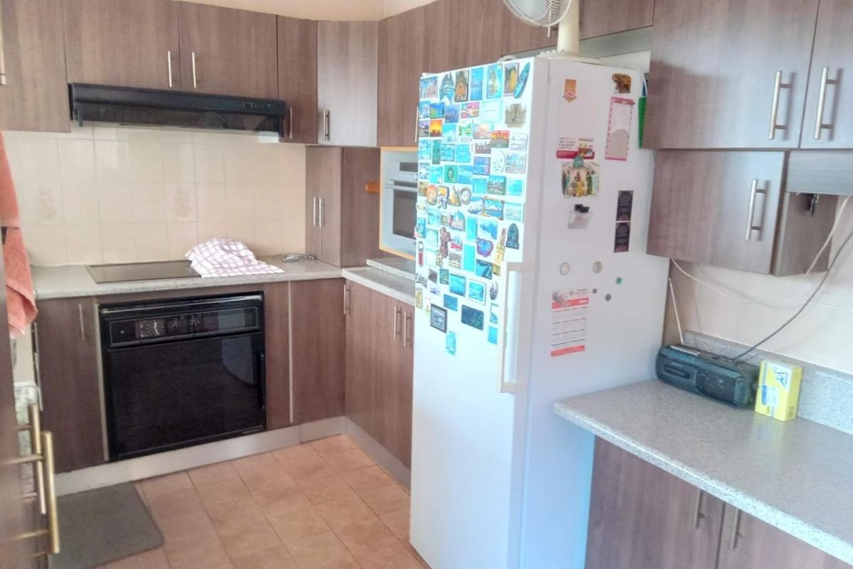 A functional kitchen featuring wood-tone laminate cabinetry, built-in oven, electric cooktop, extractor fan, and tiled splashback with ample counter space.