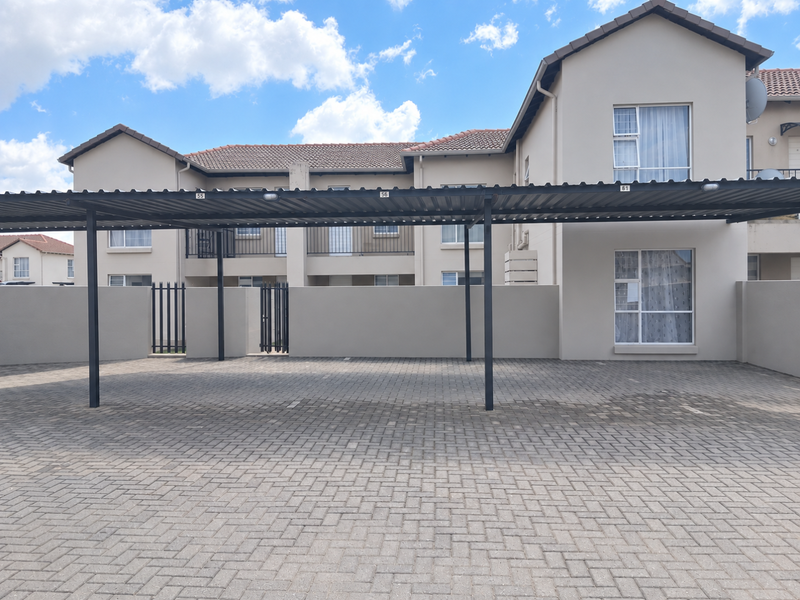 A well-maintained townhouse exterior featuring a covered carport, paved driveway, and secure perimeter walling with gated access.