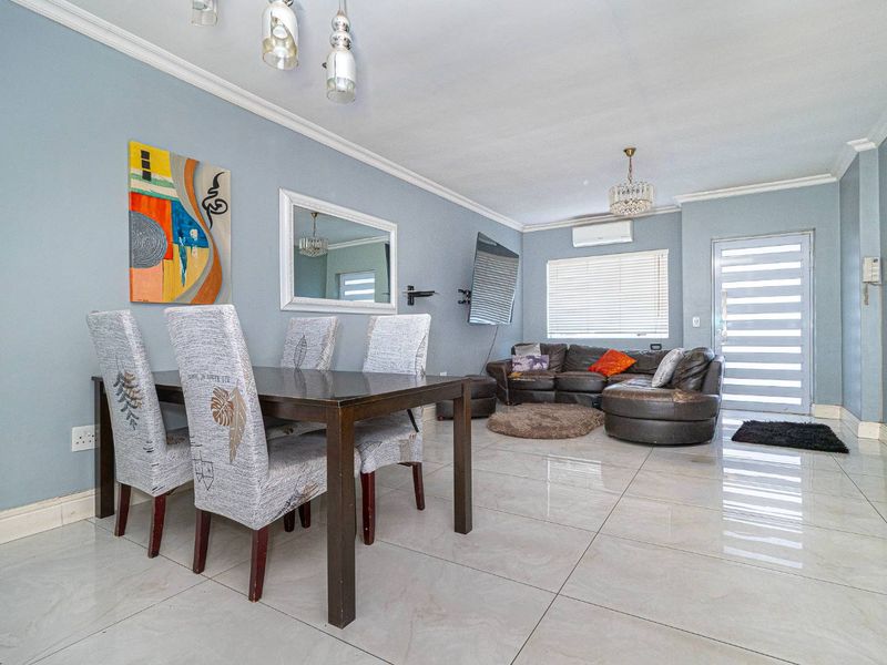 Open-plan living and dining area featuring polished porcelain floor tiles, cove cornicing, and a wall-mounted air conditioning unit.