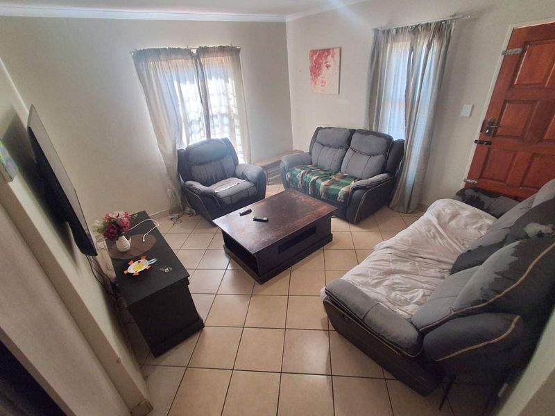A functional living room featuring ceramic floor tiles, a timber entrance door, and coved ceiling cornices, providing a comfortable and practical living space.