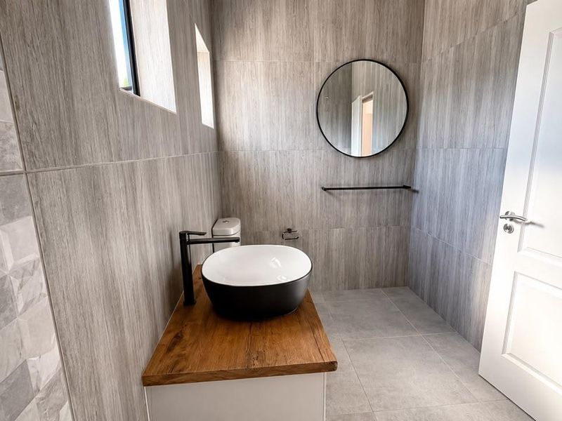 Modern bathroom featuring a vessel sink on a wooden vanity top, complemented by contemporary grey wall tiles and black fixtures.