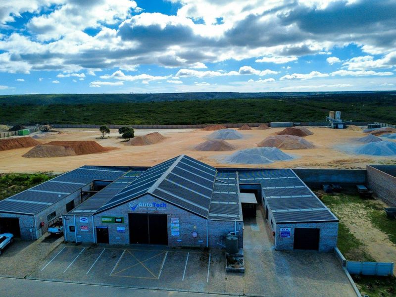 Aerial view of a commercial workshop facility featuring a large corrugated metal roof, brick exterior, and an expansive paved parking and storage yard.
