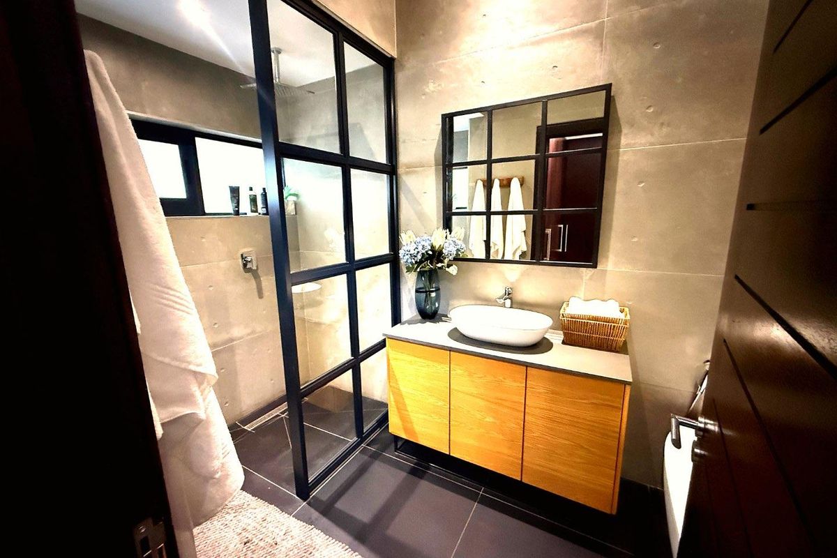 Modern bathroom featuring a concrete-look tiled wall, a floating timber vanity with a vessel sink, and a black-framed glass shower enclosure.