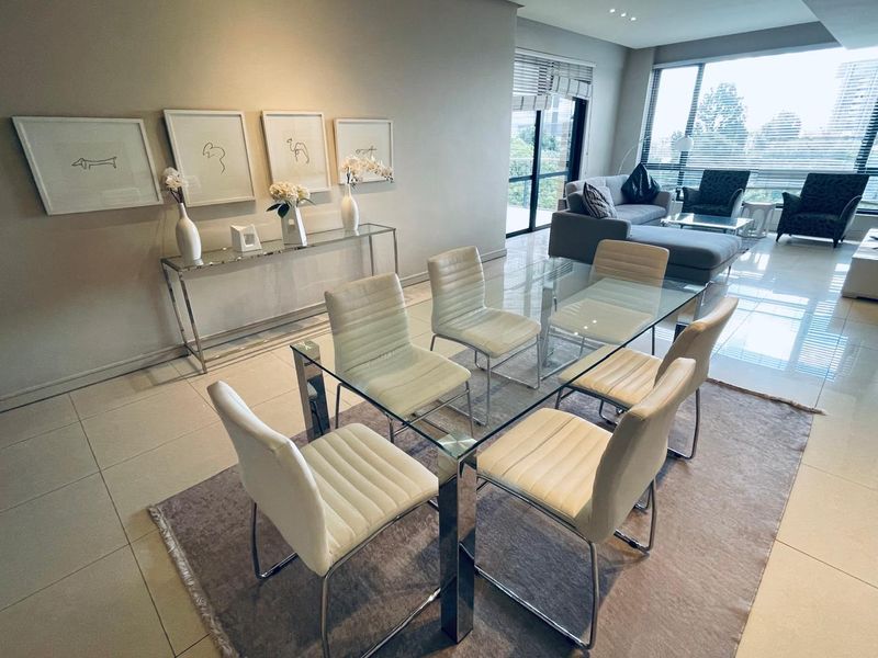 A bright and modern open-plan living and dining area featuring large windows, neutral tiled flooring, and recessed lighting, creating a spacious and inviting atmosphere.