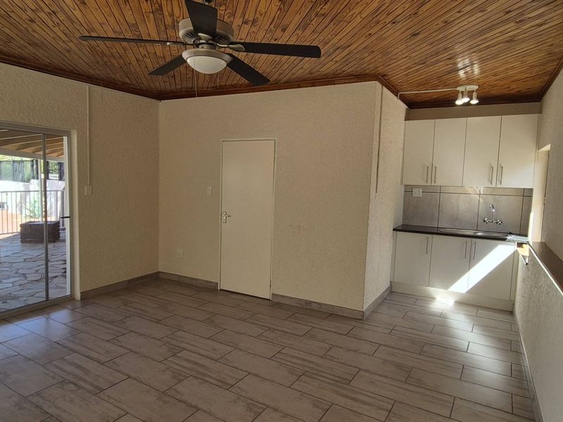 Open plan living area featuring a timber ceiling, tiled floors, and a compact kitchenette with built-in cabinetry, leading out to a patio area.