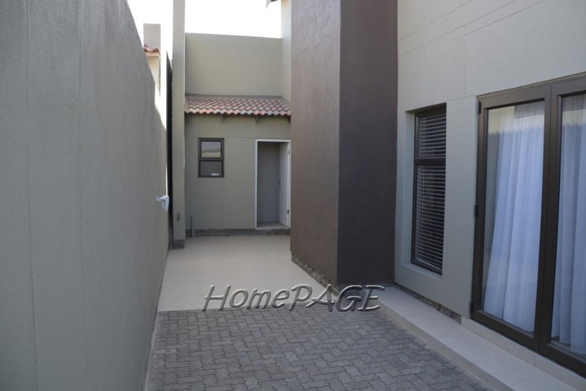 A side exterior walkway featuring paved flooring, modern dark-framed windows, and a rear access door, providing a clean and functional outdoor transition space.