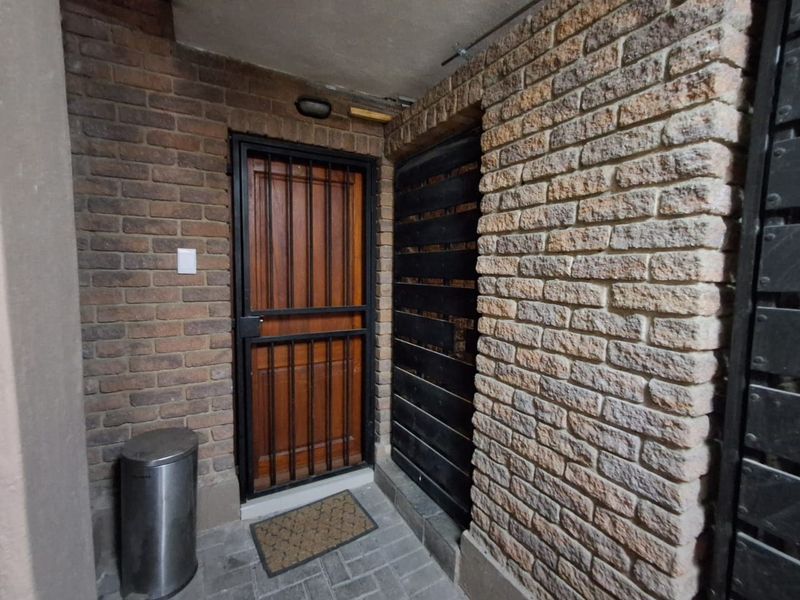 A secure apartment entrance featuring exposed brick walls, a timber door with a metal security gate, and durable paved flooring.