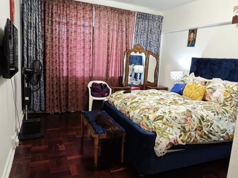 A bedroom featuring dark parquet flooring and large window curtains, providing a functional space with potential for modern updates.