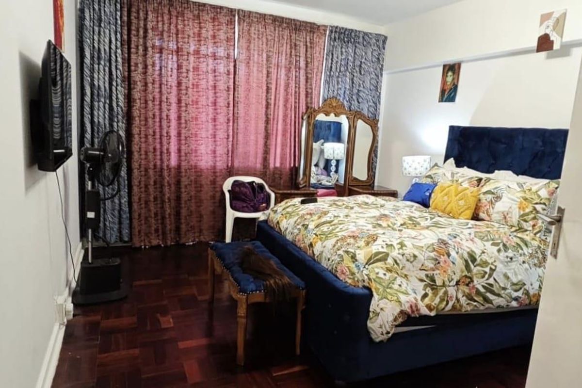 A bedroom featuring dark parquet flooring and large window curtains, providing a functional space with potential for modern updates.