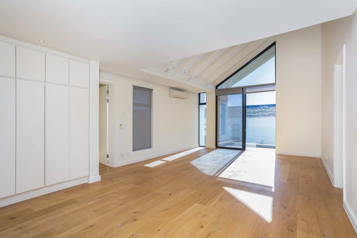 A bright, modern bedroom featuring vaulted ceilings with exposed rafters, hardwood flooring, built-in cabinetry, and large glass doors leading to an outdoor area.