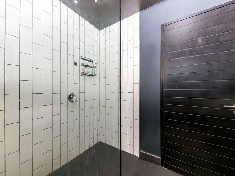 Modern bathroom shower area featuring white subway tile wall cladding, a frameless glass screen, and a dark timber door.