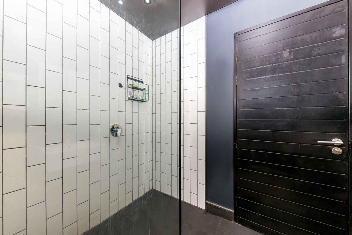 Modern bathroom shower area featuring white subway tile wall cladding, a frameless glass screen, and a dark timber door.