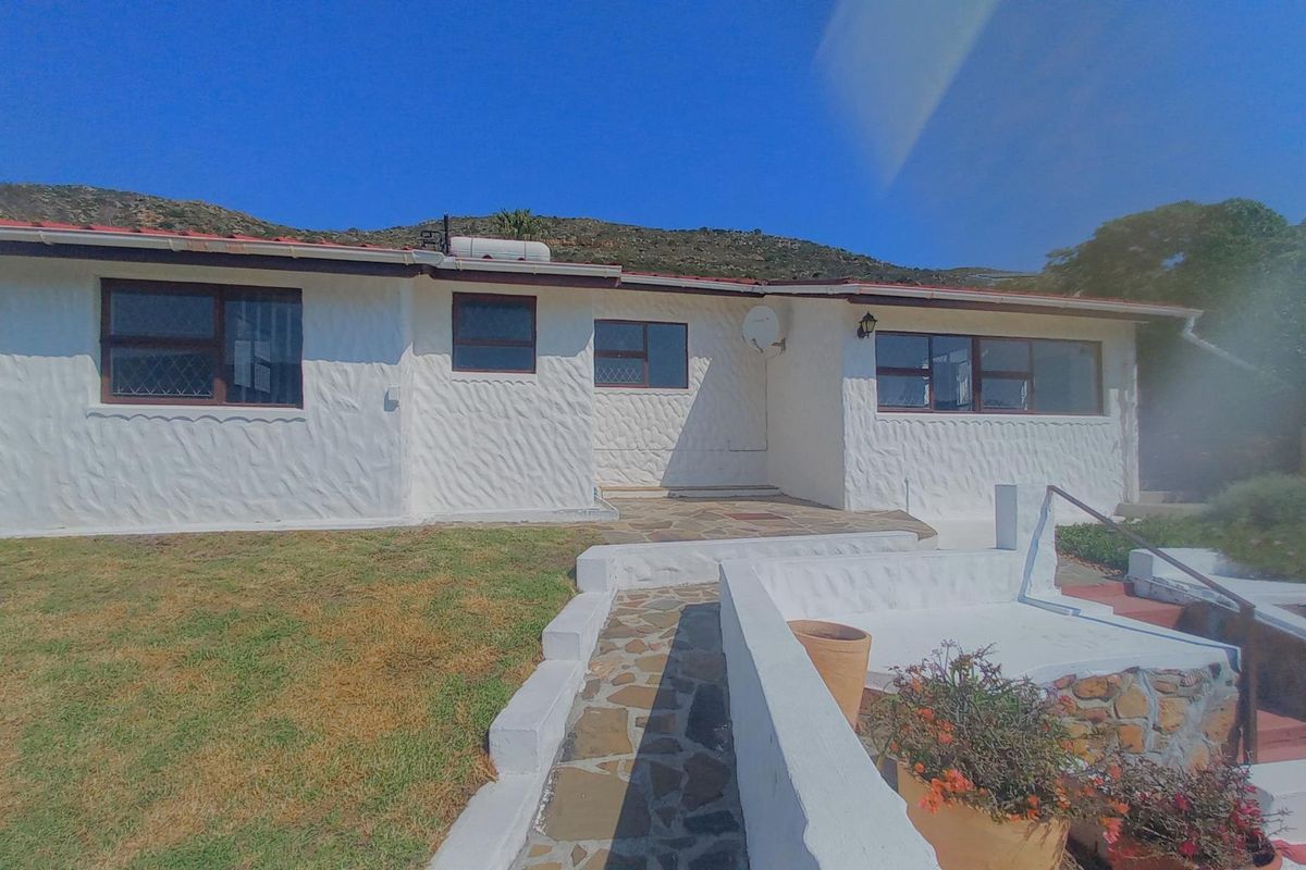 Rear view of a single-story house featuring a textured white facade, stone paved walkway, and a tiled roof with a solar water heater.