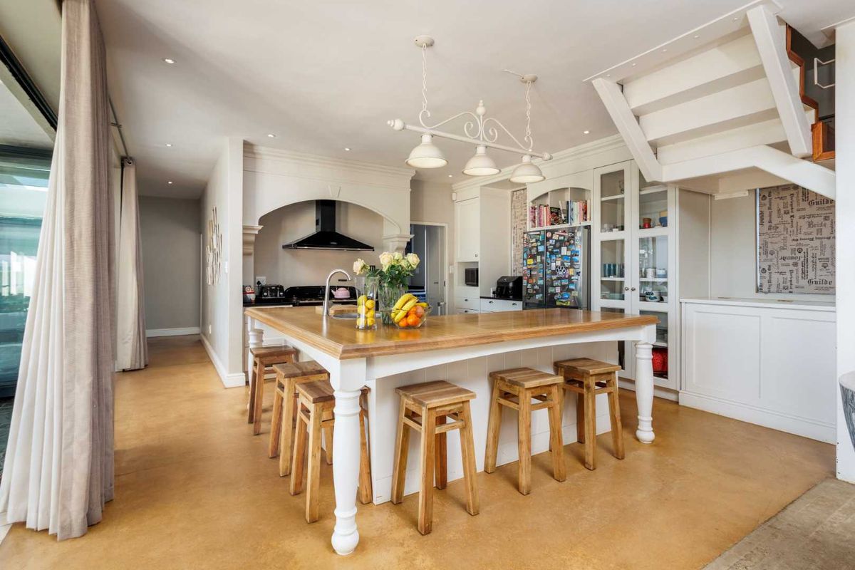 A well-appointed kitchen featuring a large central island with a wooden countertop, custom cabinetry, and an integrated staircase leading to the upper level.