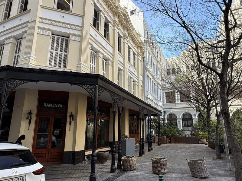 A well-maintained retail building facade featuring classic architectural detailing, a covered wrought iron veranda, and a paved outdoor courtyard area.