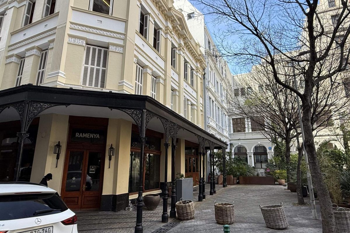 A well-maintained retail building facade featuring classic architectural detailing, a covered wrought iron veranda, and a paved outdoor courtyard area.
