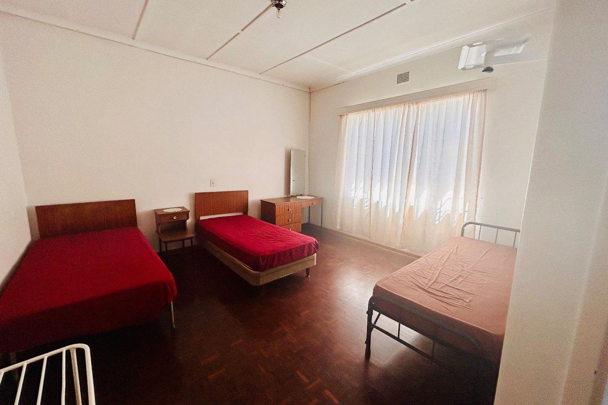 Spacious bedroom featuring original parquet flooring, large window with curtaining, and ceiling-mounted light fixture.
