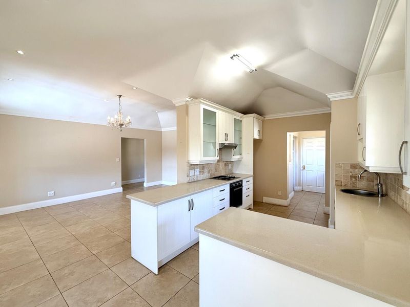 Spacious open-plan kitchen and living area featuring white cabinetry, stone countertops, built-in appliances, tiled flooring, and a vaulted ceiling with recessed lighting.