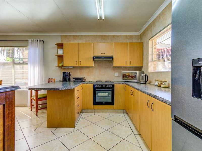A functional kitchen featuring light wood cabinetry, granite countertops, a built-in oven with extractor fan, and tiled flooring throughout.