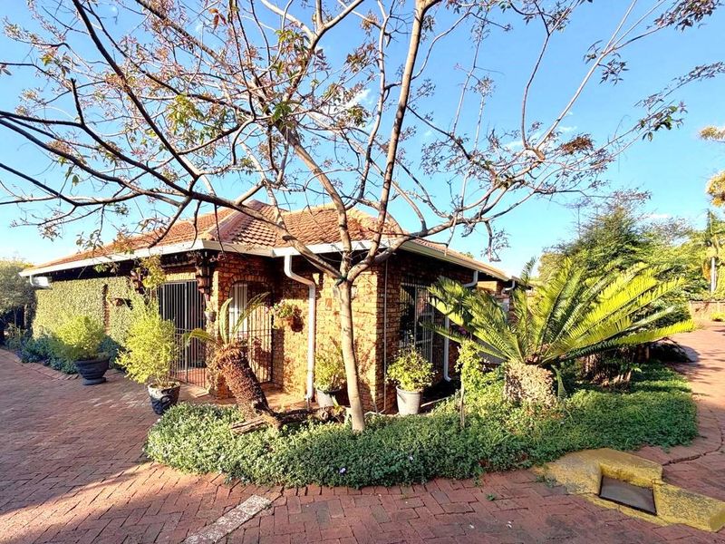 A charming brick townhouse exterior featuring a tiled roof, secure entrance gates, and a well-established garden with paved driveway access.