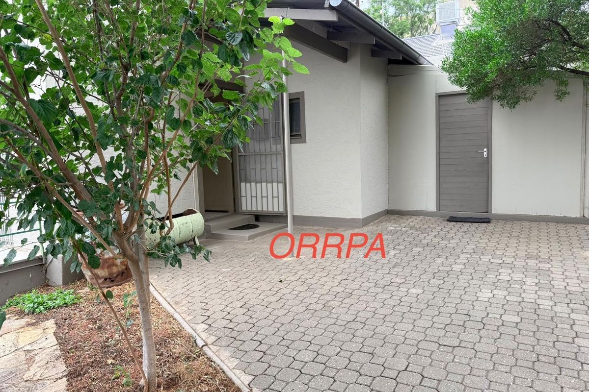 A paved rear courtyard area featuring a covered entrance and a secondary access door, providing a functional outdoor space.
