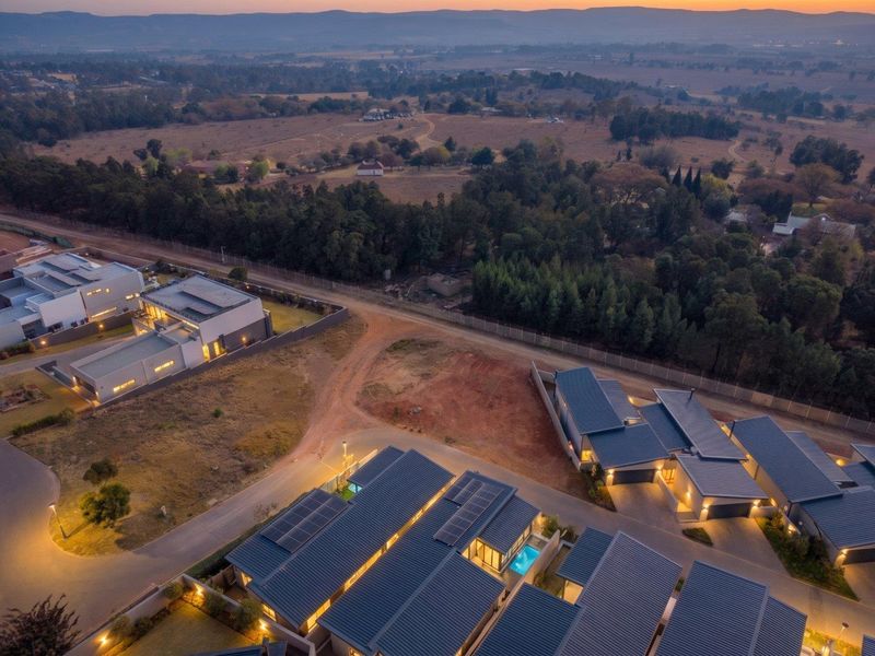 Aerial view of a modern residential estate at dusk, showcasing contemporary homes with solar panels, private pools, and surrounding landscape.