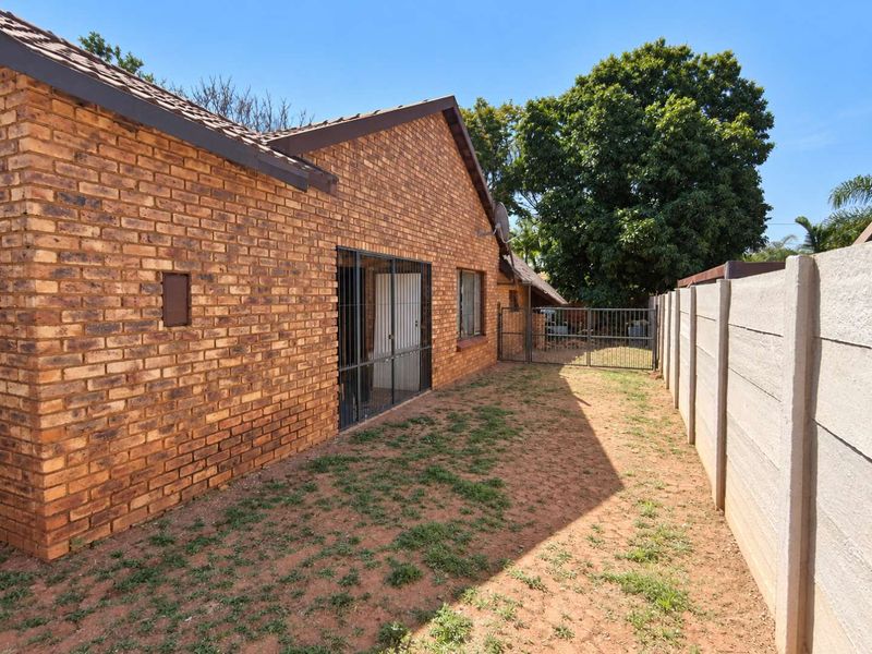 Rear view of a face brick house featuring a secure gated side passage and a precast concrete boundary wall.