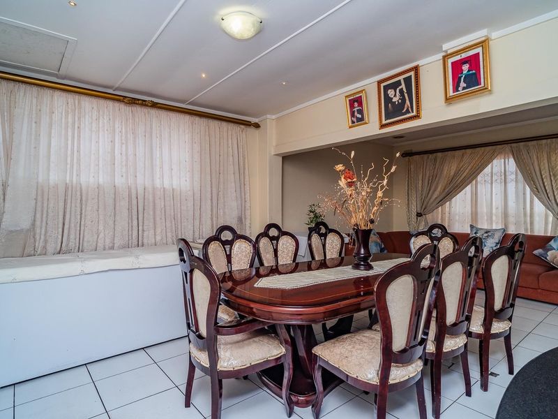 A spacious dining area featuring tiled flooring, recessed lighting, and large windows with curtain rails, providing a functional space for family meals.