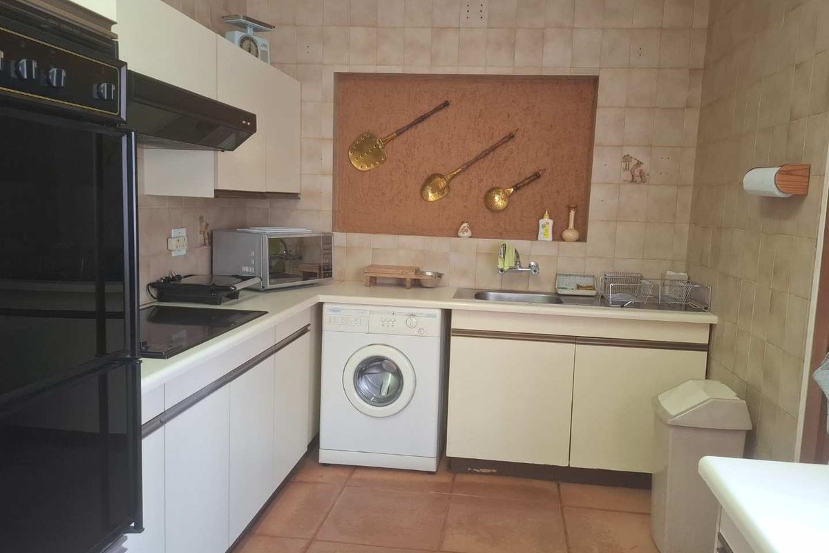 A compact, dated kitchen featuring built-in cabinetry, integrated oven, extractor fan, and a dedicated space for a washing machine.