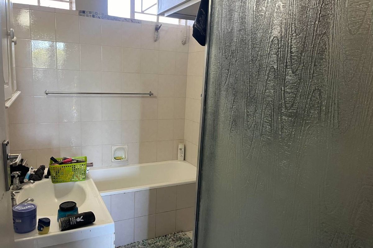 A functional bathroom featuring a built-in bathtub, vanity basin, and tiled wall finishes with a glass shower screen.